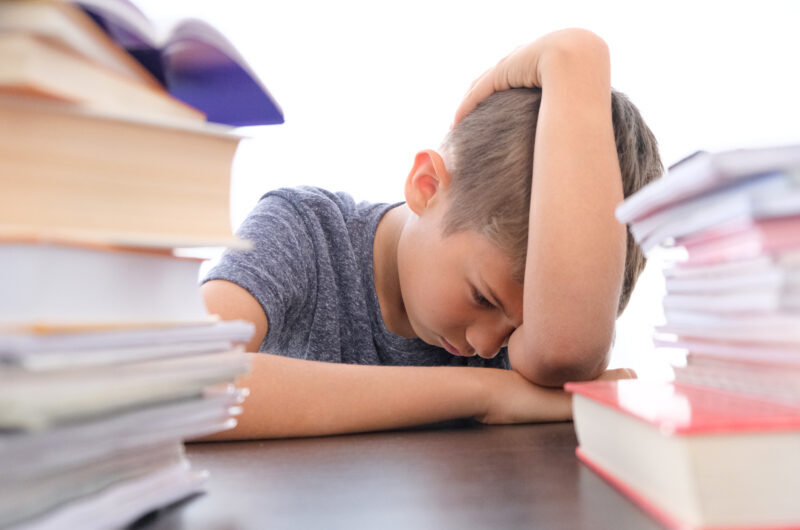 Criança aparentemente cansada em meio aos livros