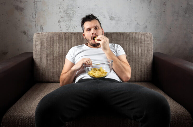 homem jogado no sofá e comendo algo que não parece saudável